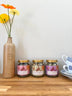 Three jars of tea with floral labels on a wooden surface next to a vase with flowers.